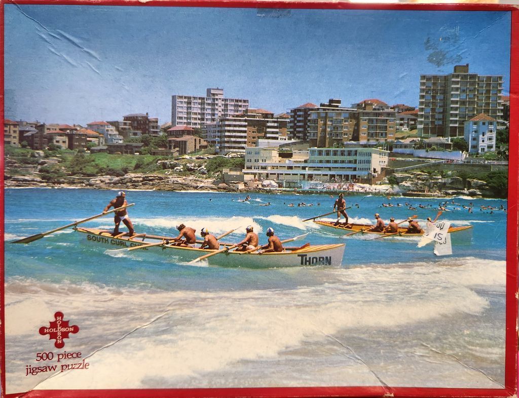 Surf boats with rowers in the ocean in front of a coastal town