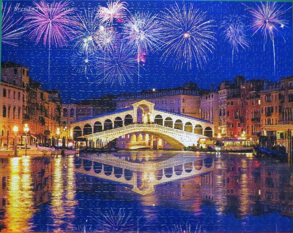 Fireworks lighting up the night sky over the Rialto Bridge in Venice reflecting on the water.