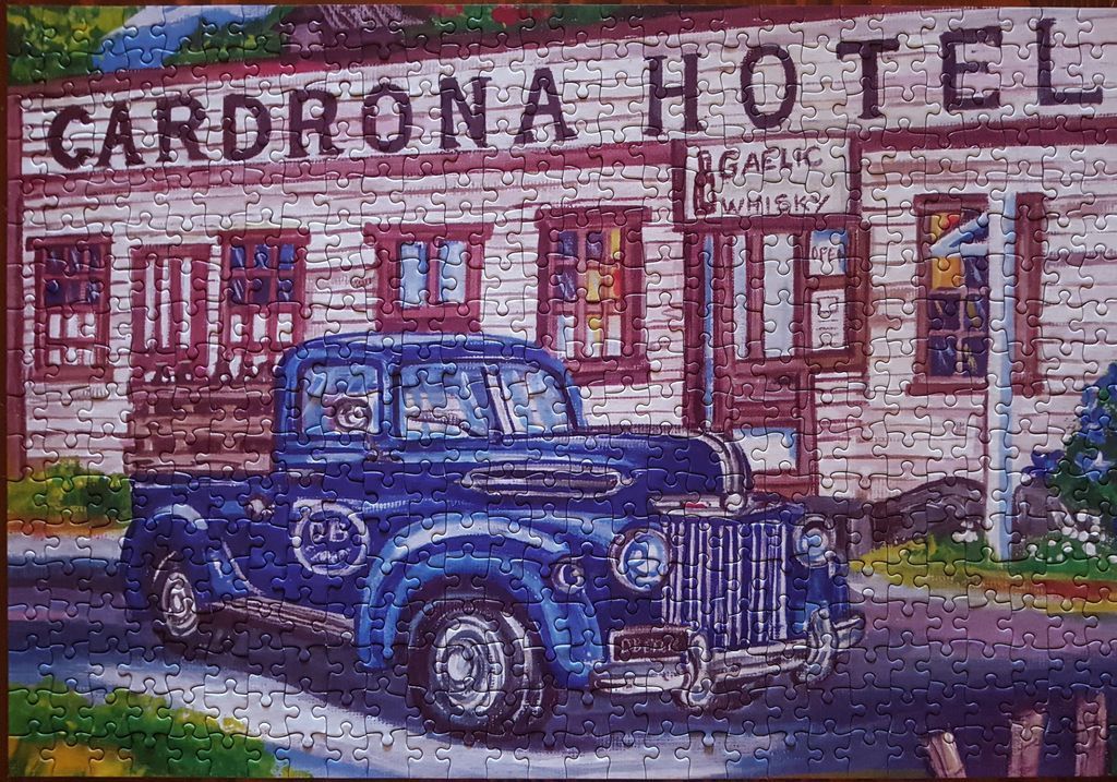 A vintage blue pickup truck parked in front of the historic Cardrona Hotel building.