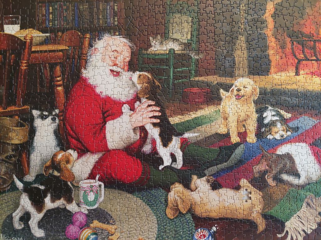 Santa Claus sitting on the floor surrounded by many playful puppies in a cozy room.