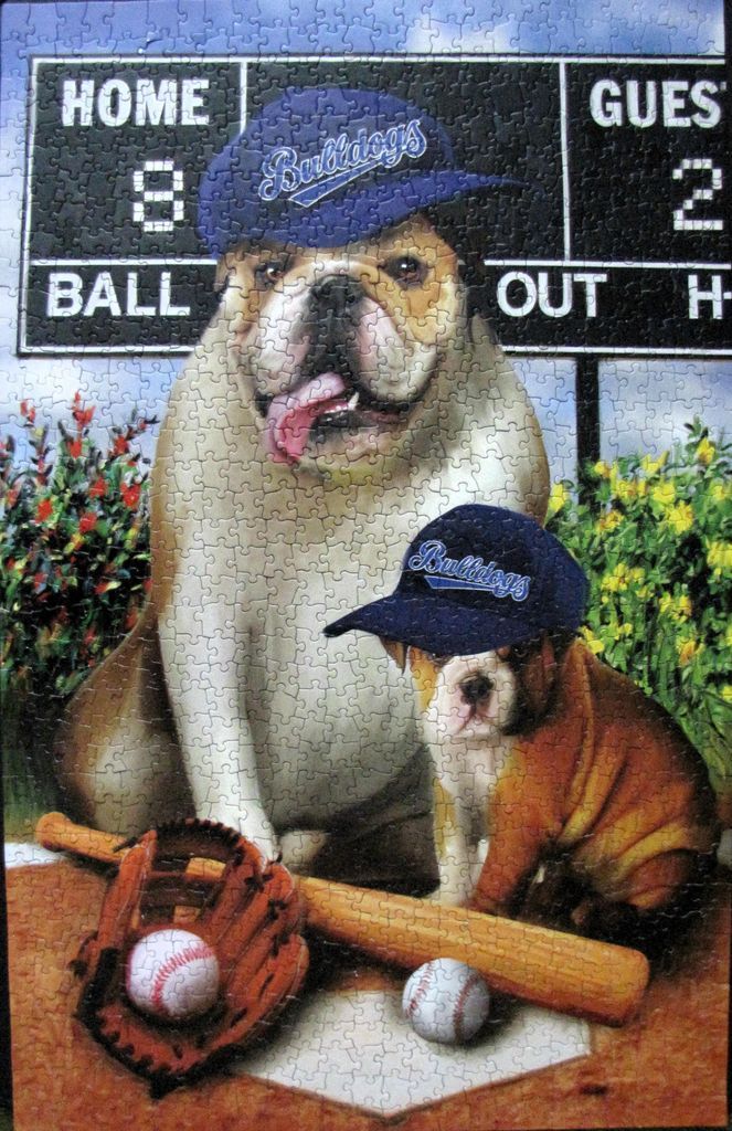Two bulldogs wearing baseball caps in front of a scoreboard on a baseball field.