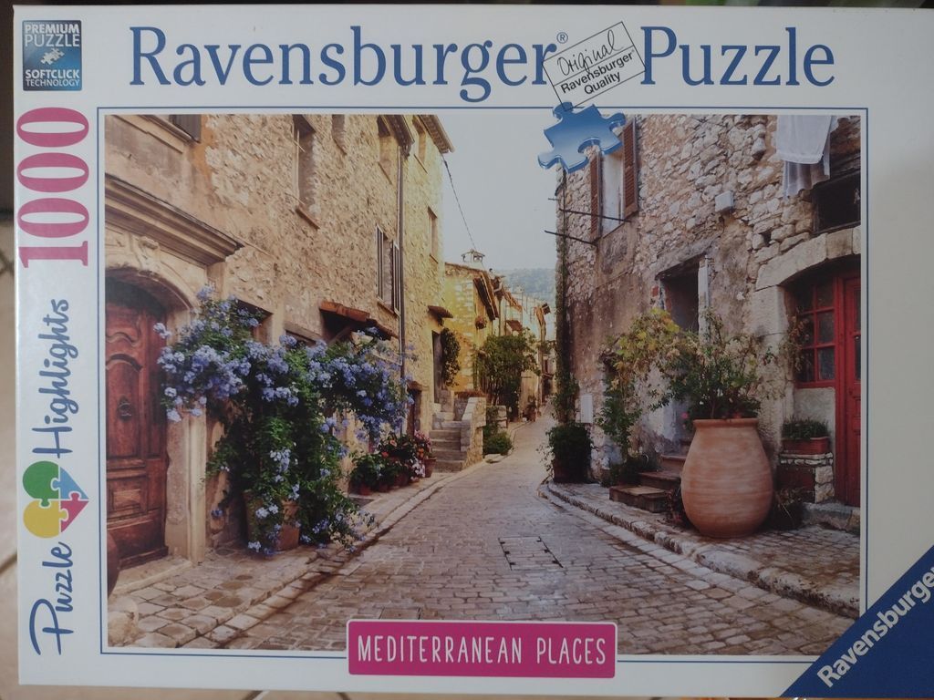 A narrow cobblestone street in a Mediterranean village lined with old stone buildings, blooming flowers, and terracotta pots.
