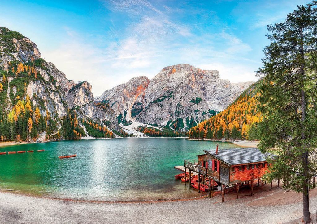 A red wooden boathouse on stilts beside a turquoise mountain lake surrounded by golden autumn trees.