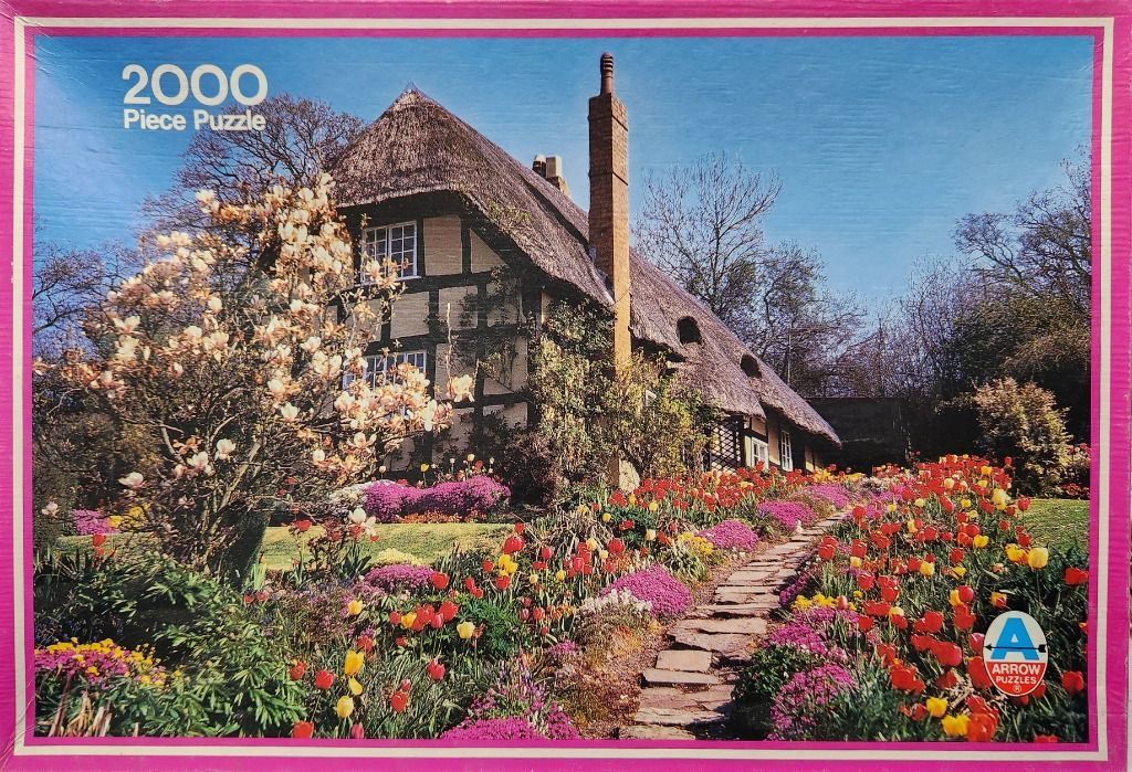 A traditional English thatched-roof cottage surrounded by a vibrant spring garden with blooming flowers.