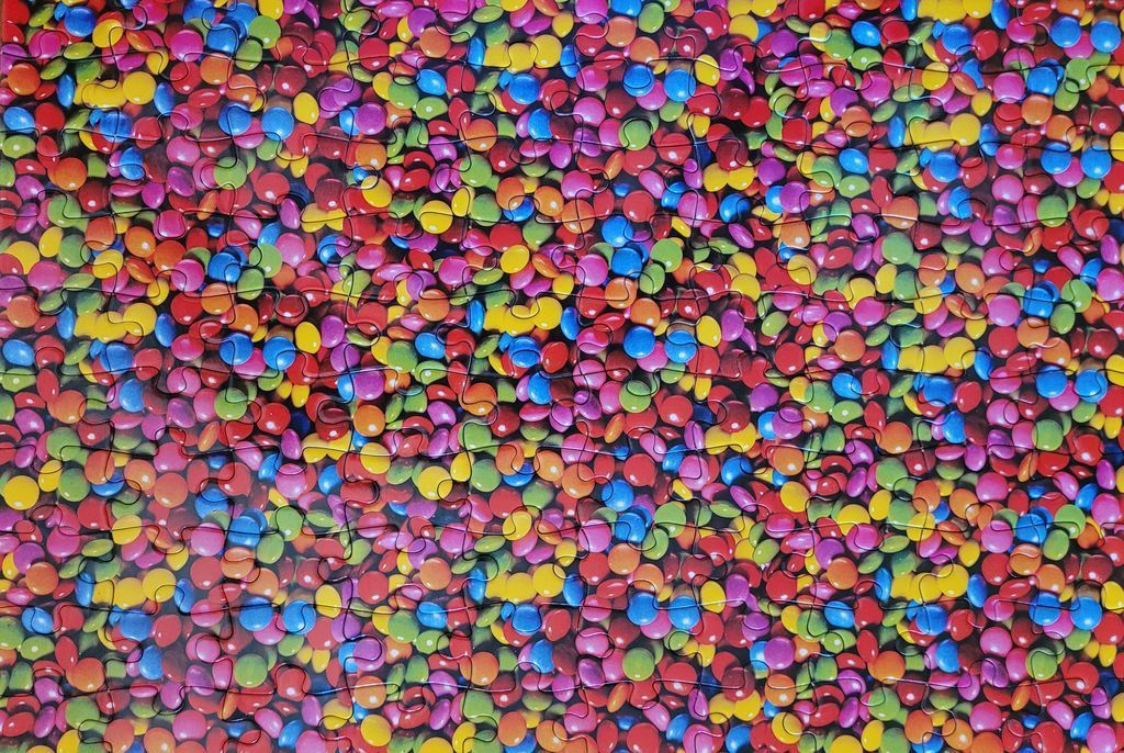 A dense, overhead pattern of colorful, circular candy-coated chocolates scattered across a surface.