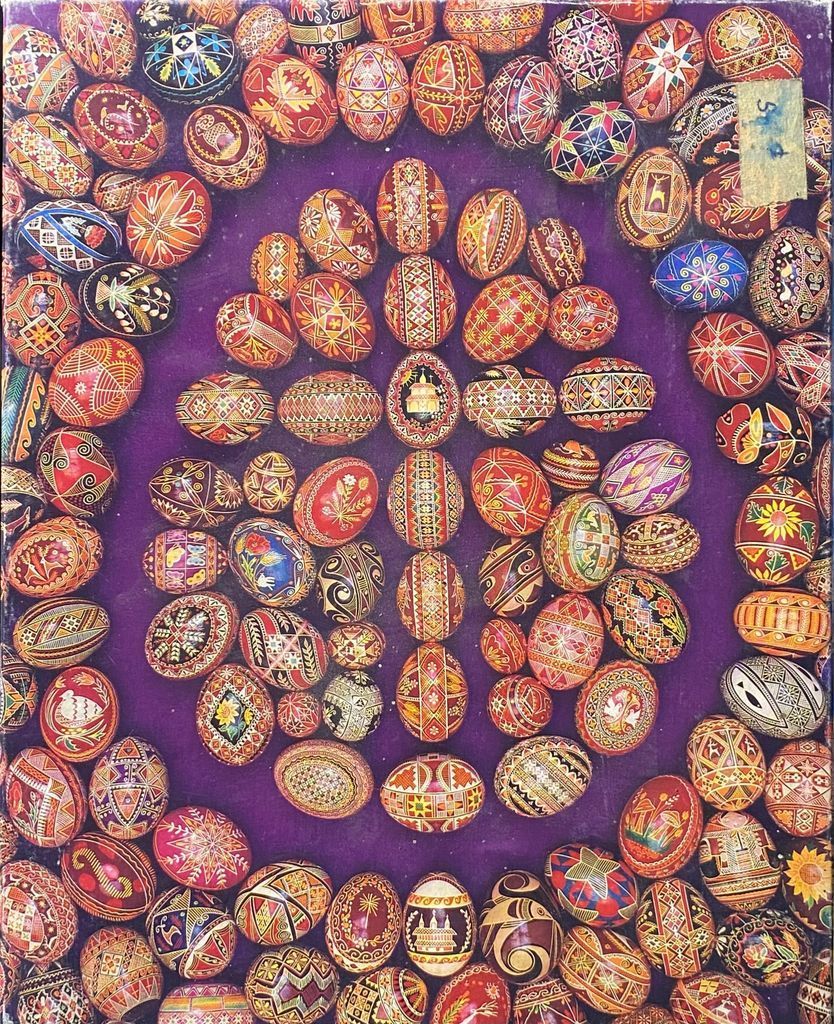 A collection of many intricately decorated Pysanky eggs arranged on a deep purple velvet background.