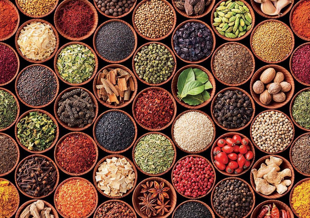 Top-down view of many small round wooden bowls filled with a colorful variety of spices, seeds, and dried herbs.