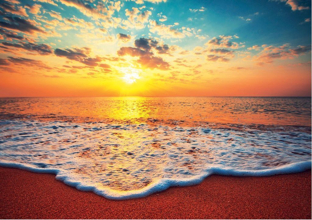 A vibrant sunset over a calm ocean washing onto a sandy beach