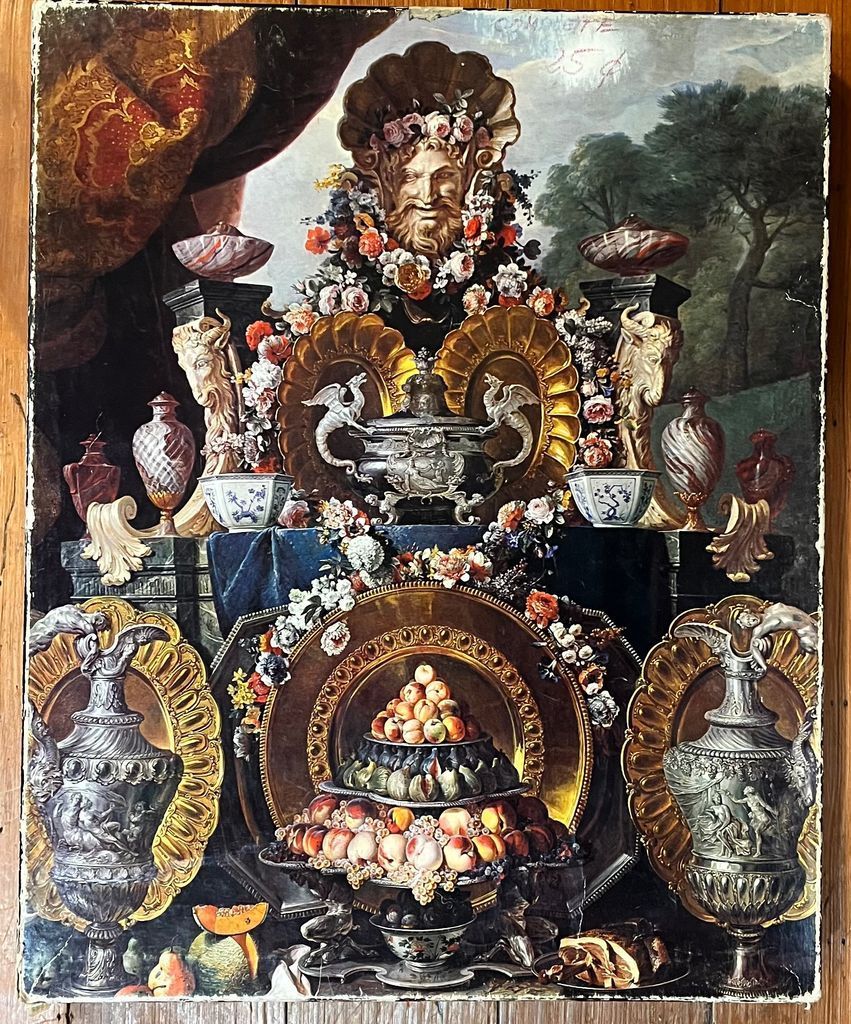 An ornate Baroque-style still life painting featuring fruit, silver urns, and a central face mask sculpture.