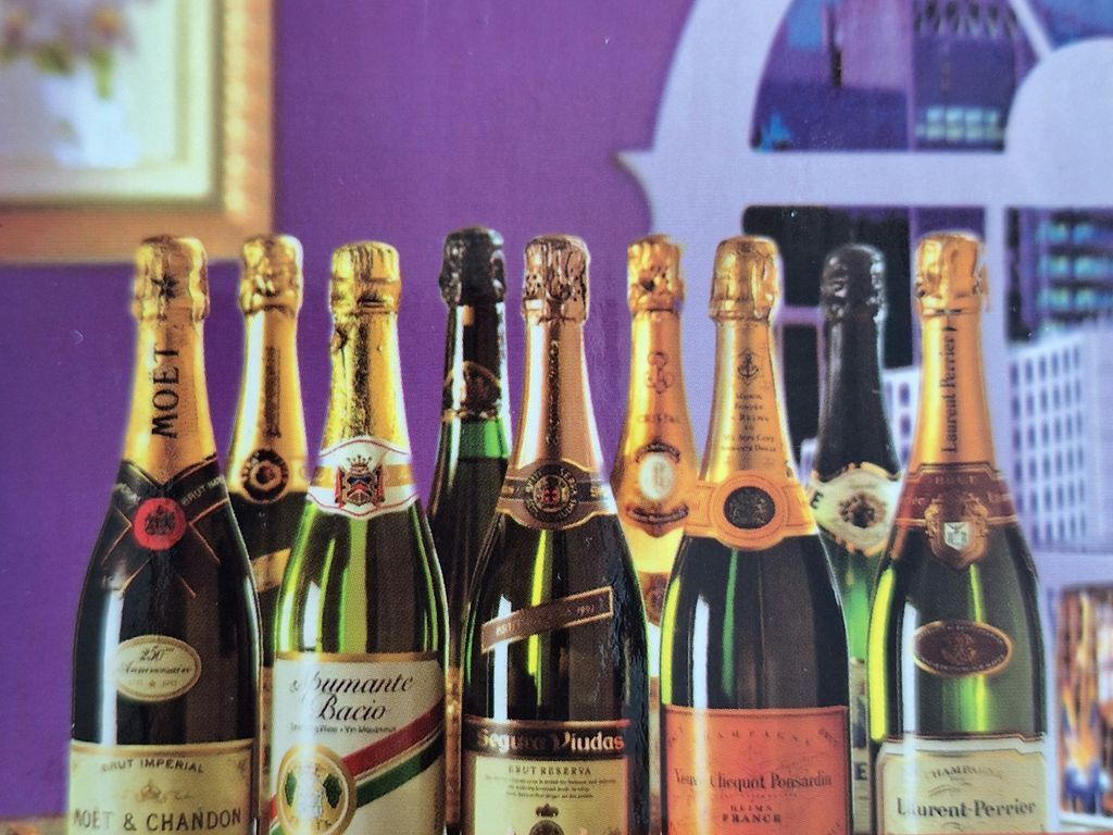 A row of nine champagne and sparkling wine bottles arranged against a deep purple wall.
