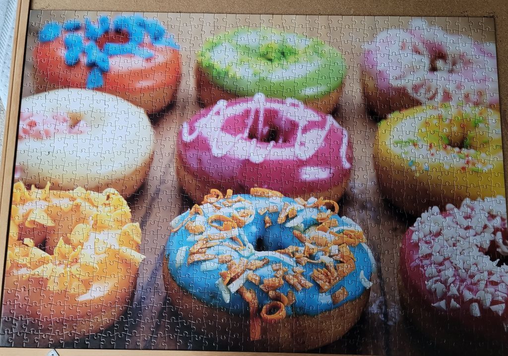 A grid of eight vibrant, colorful glazed donuts arranged on a dark wooden surface.
