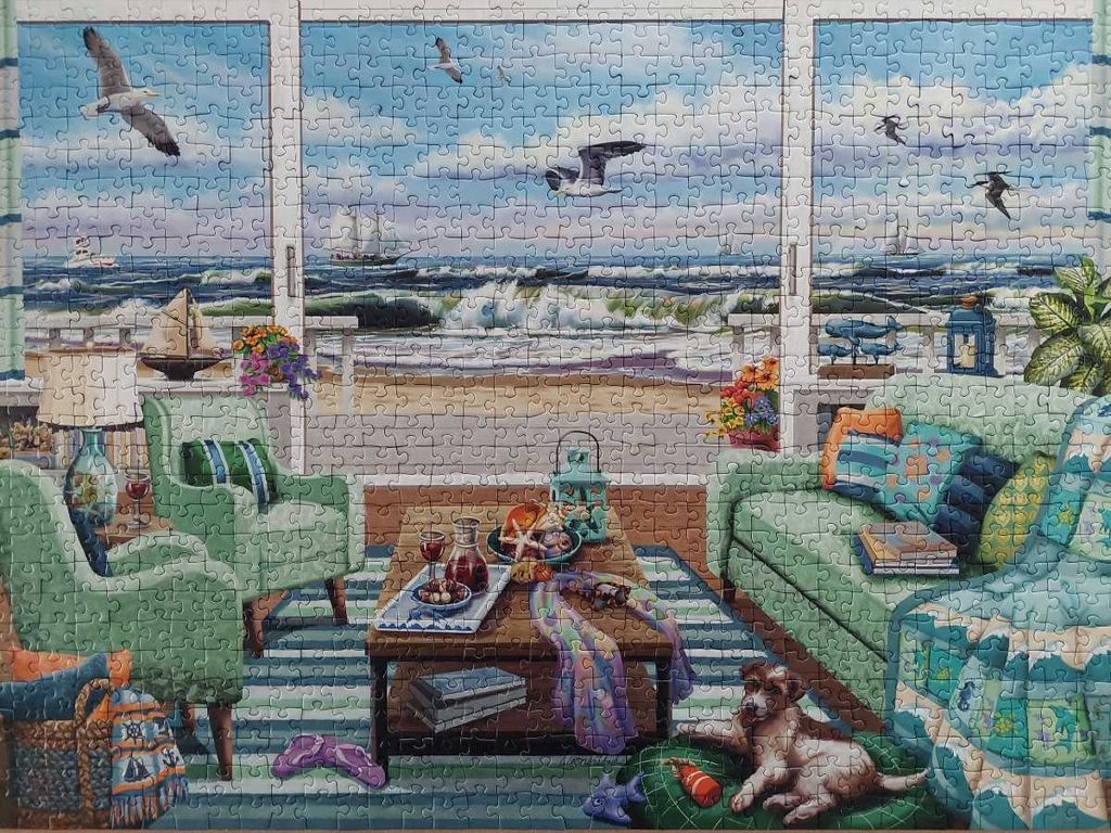 A cozy living room view overlooking a beach and ocean through large windows.