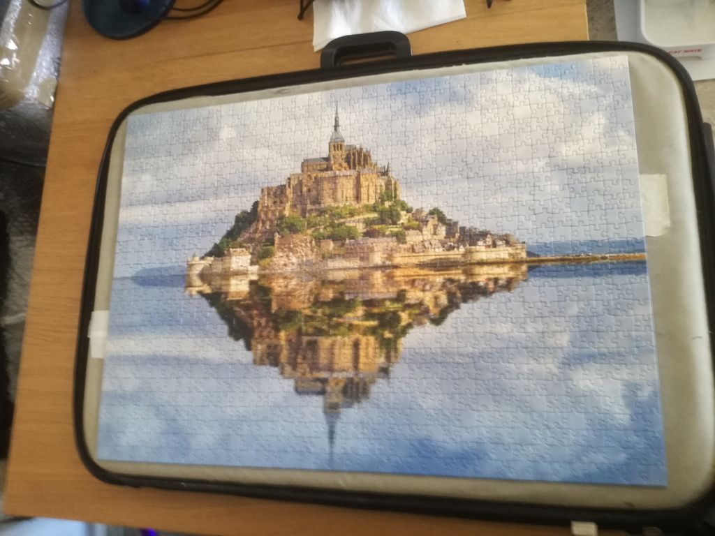 Mont Saint-Michel Abbey reflecting in calm tidal waters under a bright sky.