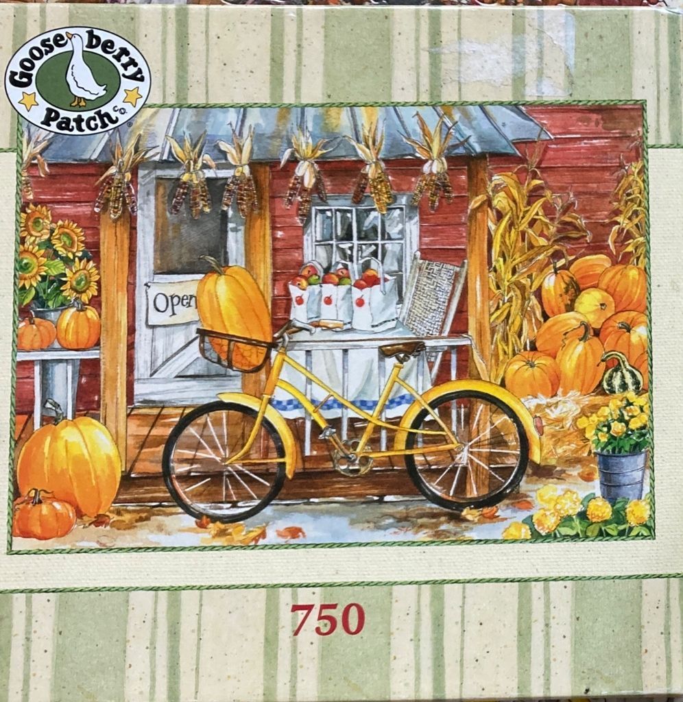 A bright yellow bicycle with a large pumpkin in its front basket parked in front of a rustic red farm building in autumn.