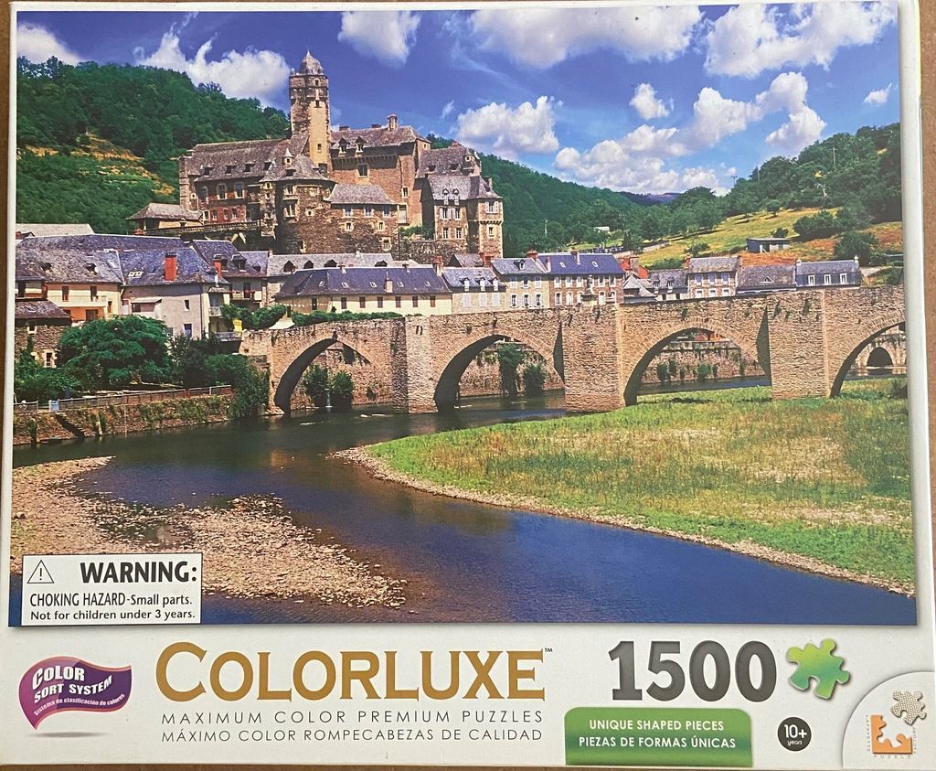 A European village with a stone castle and multi-arched bridge over a river on a sunny day.