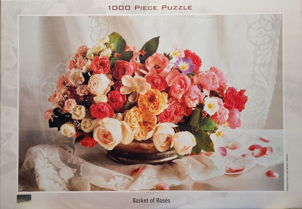 A lush bouquet of various roses in a metal bowl sitting on a lace-covered table.