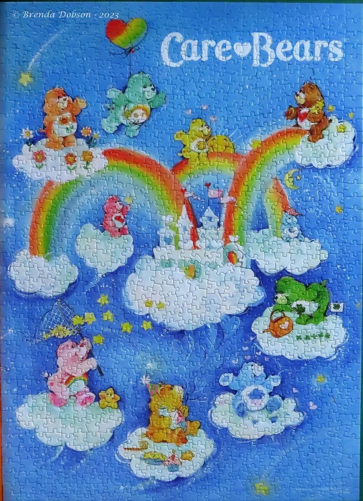 A whimsical illustration of various colorful Care Bears playing on clouds under rainbows against a bright blue sky.