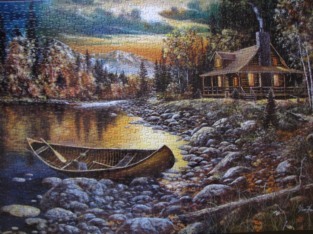 A cozy log cabin nestled by a calm lake with a wooden boat moored on the rocky shoreline at sunset.