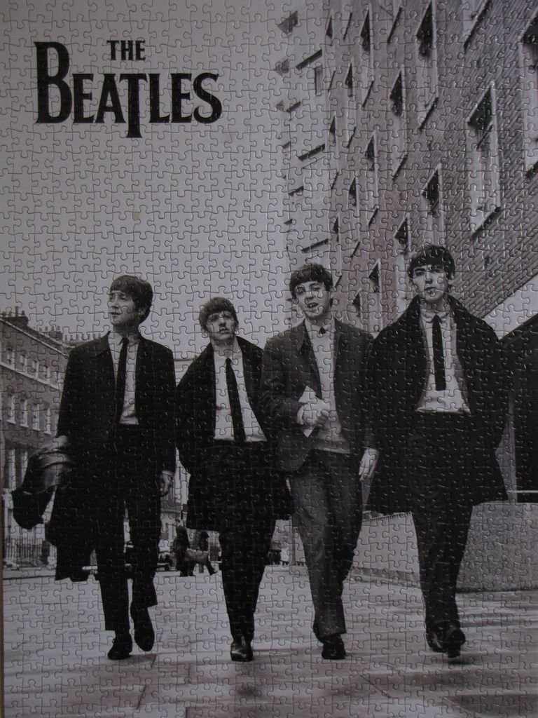 A black and white photograph of The Beatles walking down a city street.