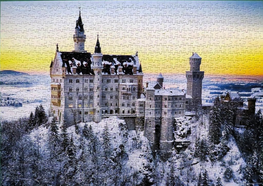 A snow-covered Neuschwanstein Castle perched on a mountain peak against a vibrant sunset sky.
