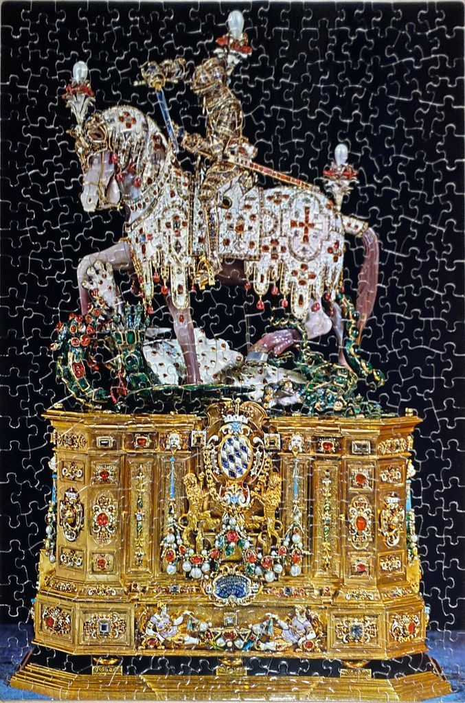 An ornate golden statuette of Saint George on horseback atop an elaborate gold pedestal against a black background.