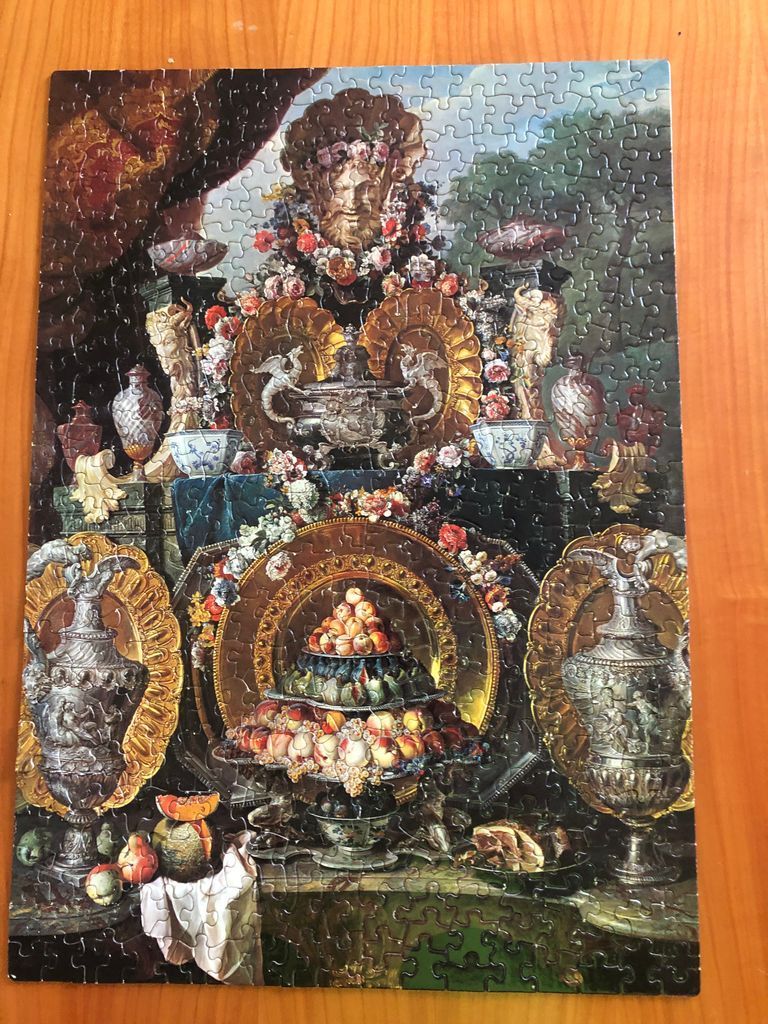 An opulent, classical-style still life featuring metallic platters, decorative urns, and a tiered arrangement of fruit.