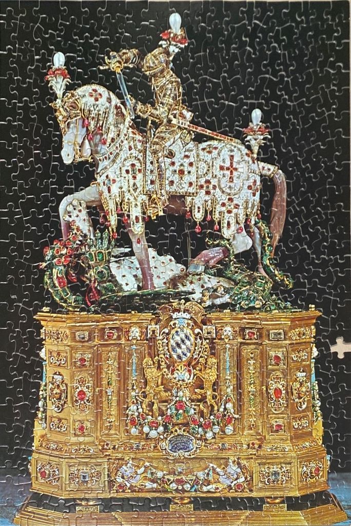 A jeweled figurine of Saint George on horseback slaying a dragon, set on an ornate golden pedestal.