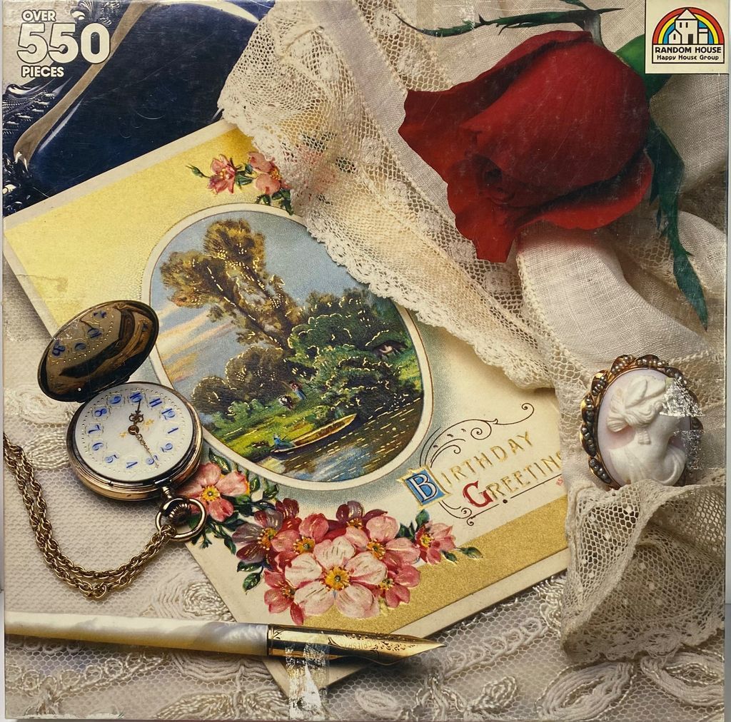 A still life featuring a vintage birthday card, a pocket watch, a single red rose, and a cameo brooch on lace.