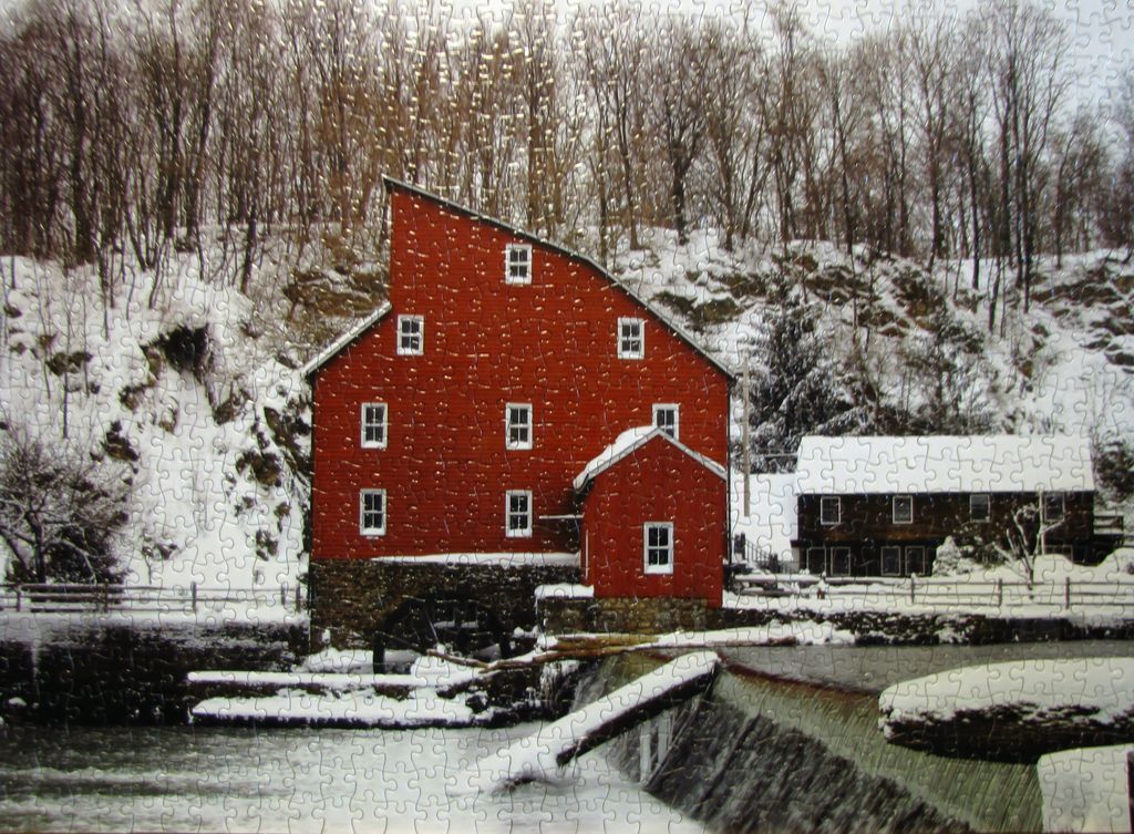 A red grist mill by a waterfall in a winter forest setting.