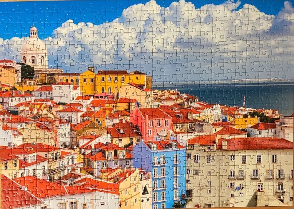 View of Lisbon, Portugal featuring a white domed church, terracotta rooftops, and colorful buildings against a blue sky.