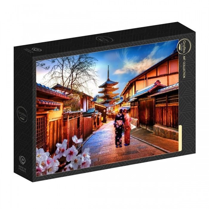 Two women in kimonos walking down a narrow street in Kyoto towards a pagoda under a clear blue sky.