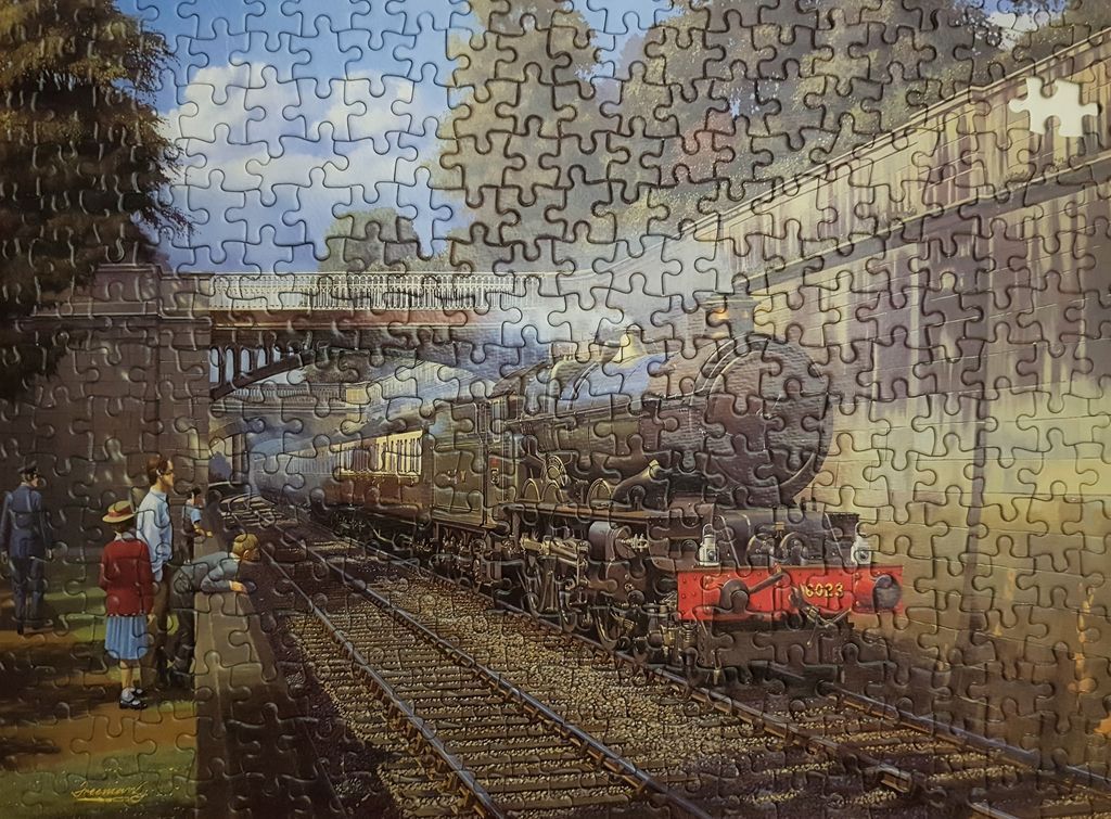 A vintage steam locomotive at a station with passengers waiting on the platform.
