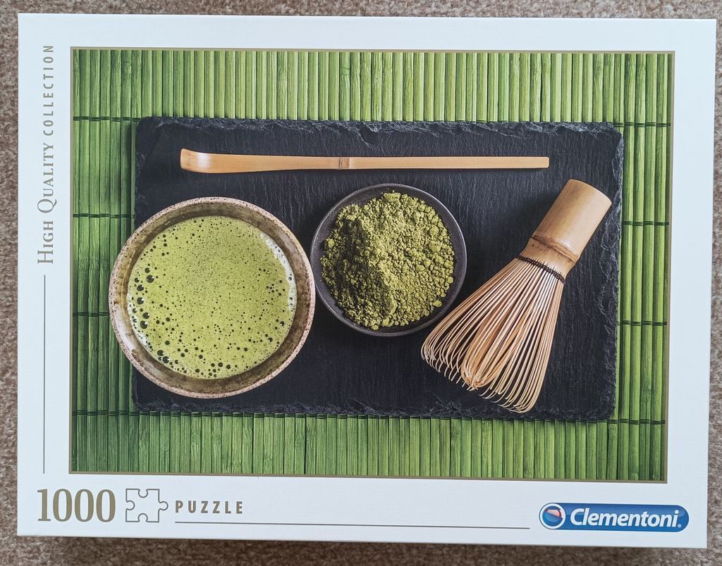 A top-down view of matcha tea preparation featuring a bowl of whisked tea, matcha powder, a bamboo whisk, and a scoop.