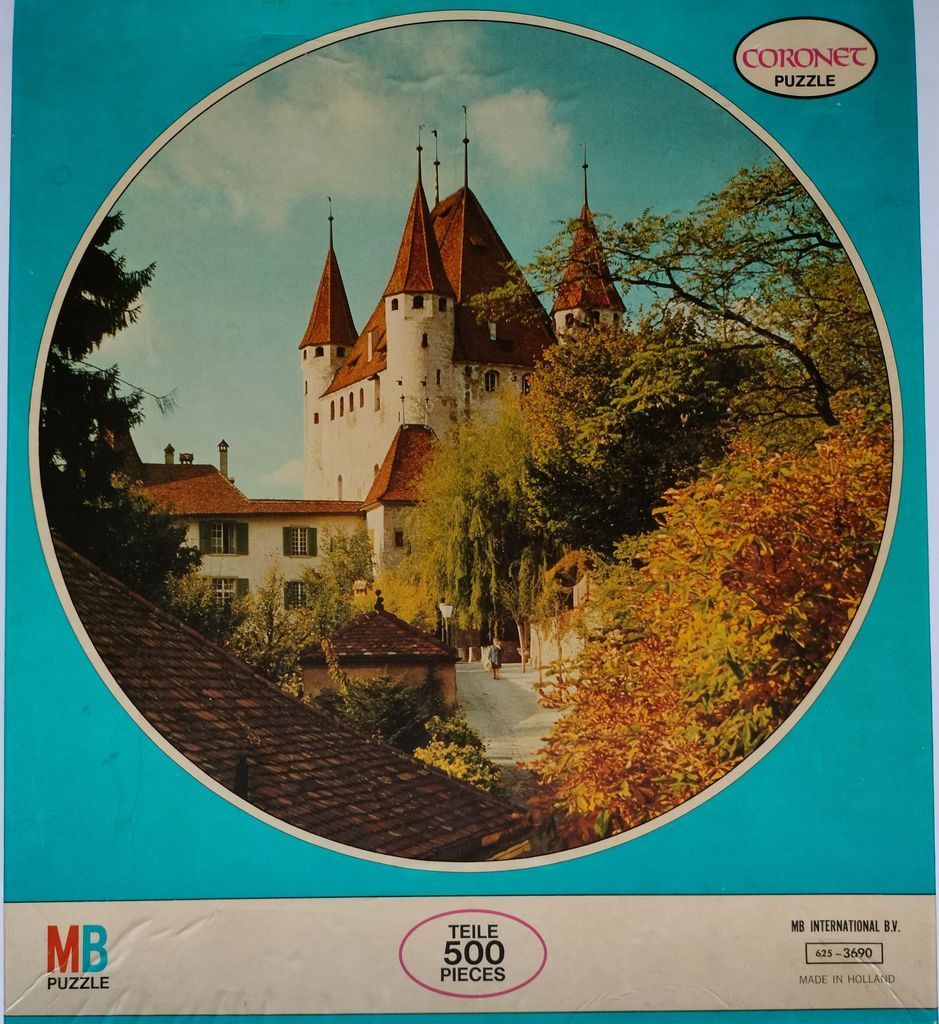 A circular photograph showing a historic Swiss castle with red-tiled roofs surrounded by lush trees.