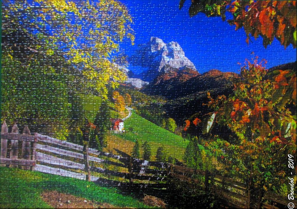 An Alpine landscape with a snow-capped peak, autumnal trees, and a wooden fence in the foreground.