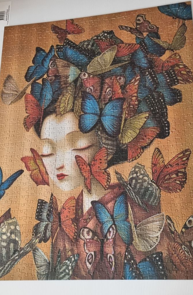 A portrait of a woman whose hair is made of many colorful butterflies against a warm, ochre background.
