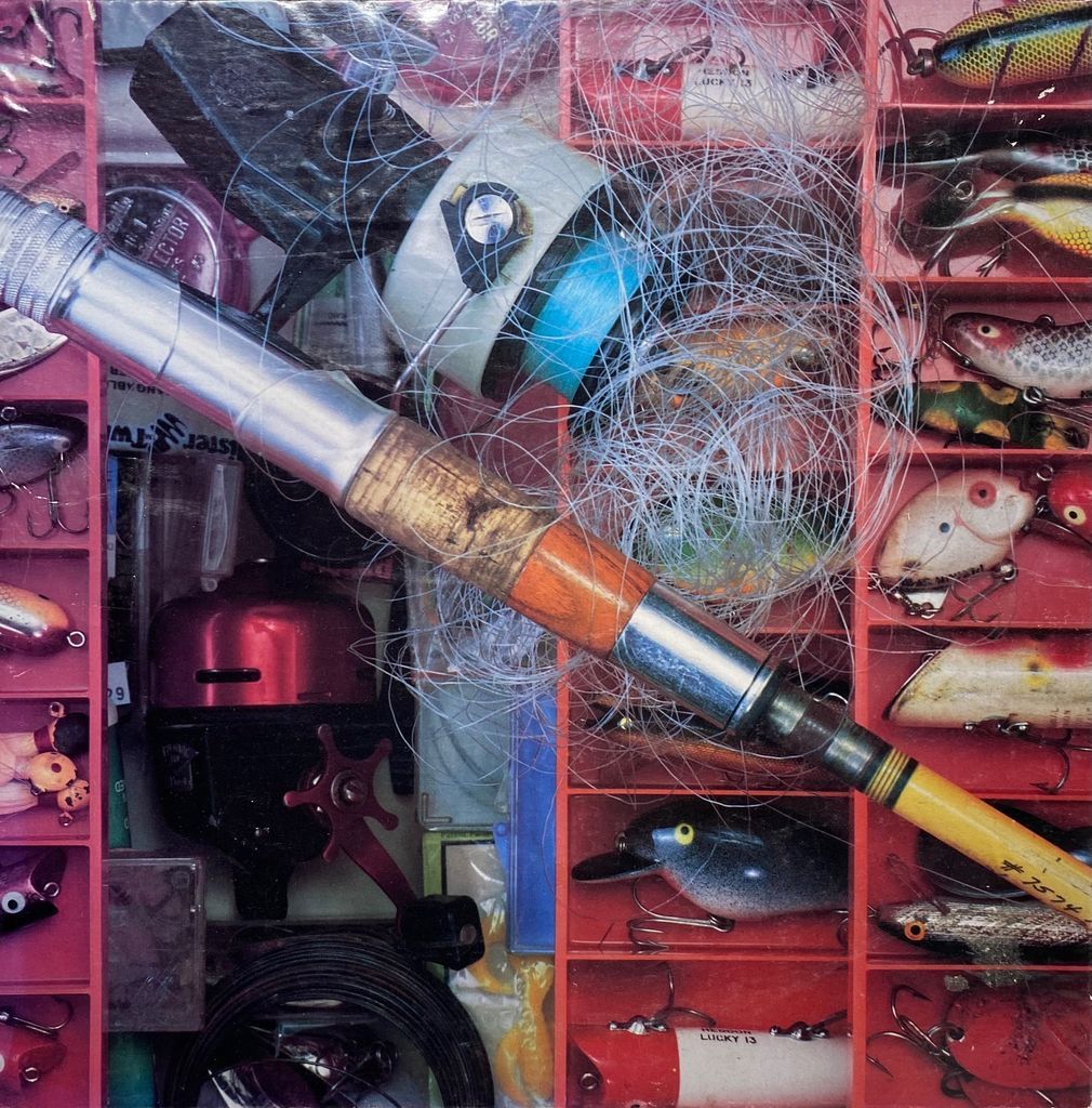 Overhead view of a fishing tackle box filled with colorful lures, reels, and a fishing rod with tangled line.