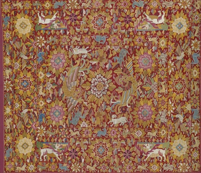 A densely patterned textile featuring mythical creatures, phoenixes, and stylized floral motifs on a deep red background.