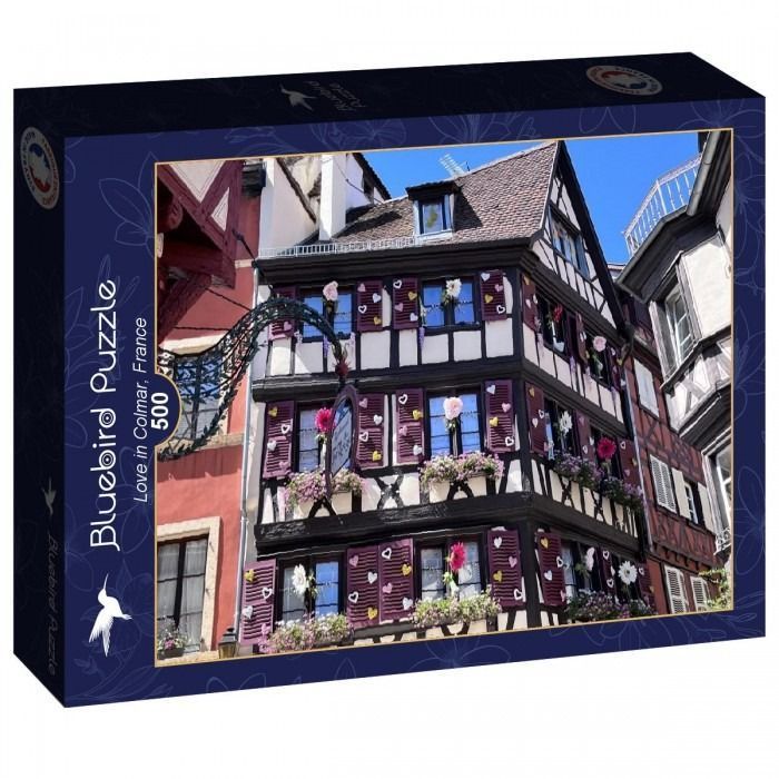 A low-angle view of a traditional half-timbered building in Colmar, France, decorated with hearts and flowers.