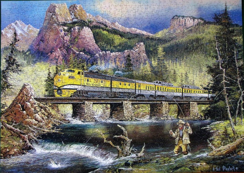 A yellow and silver passenger train crosses a stone bridge over a mountain stream while a fisherman casts his line.