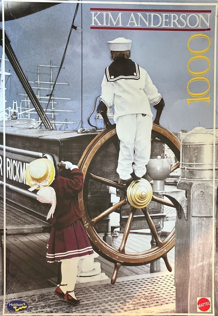A young child dressed as a sailor stands at a ship's wheel with a smaller child in a straw hat standing beside them.