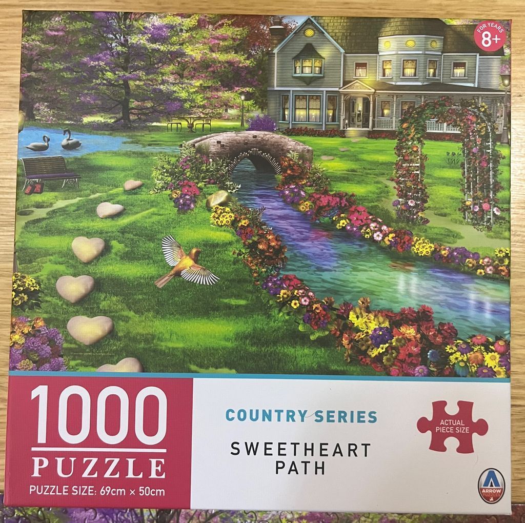 A Victorian house overlooks a garden with a stream, stone bridge, heart-shaped stepping stones, and a flying bird.