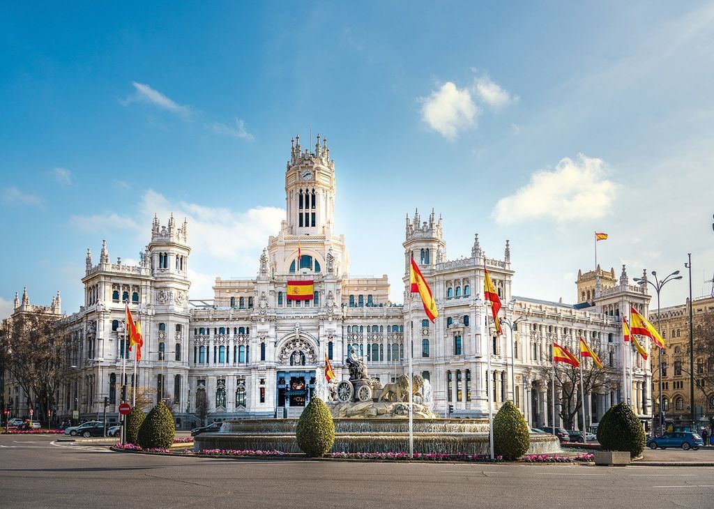 Cibeles Palace and fountain in Madrid on a sunny day with Spanish flags flying.