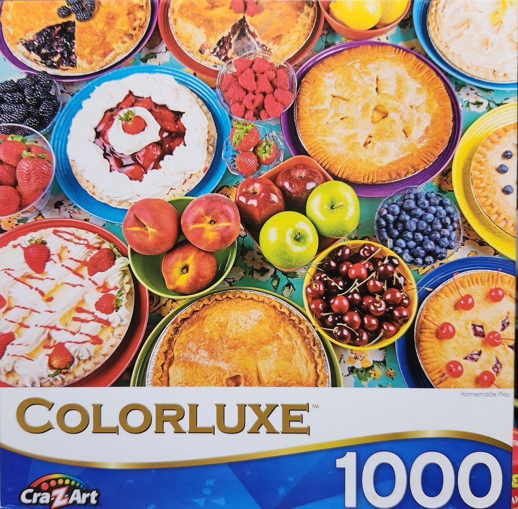 A top-down assortment of fruit pies, bowls of fresh berries, apples, and peaches on a floral tablecloth.