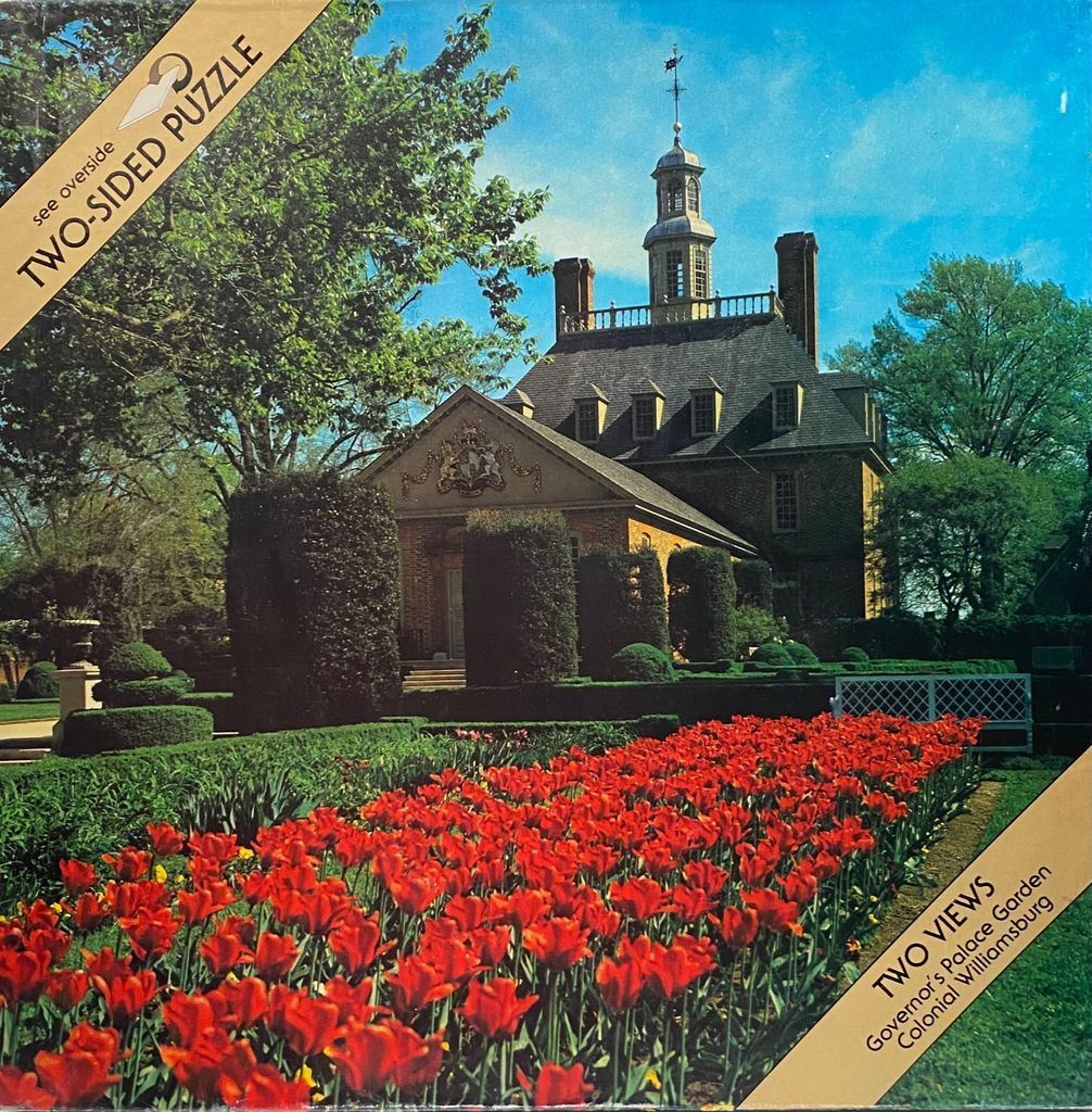 A stately brick colonial mansion behind a formal garden filled with vibrant red tulips.