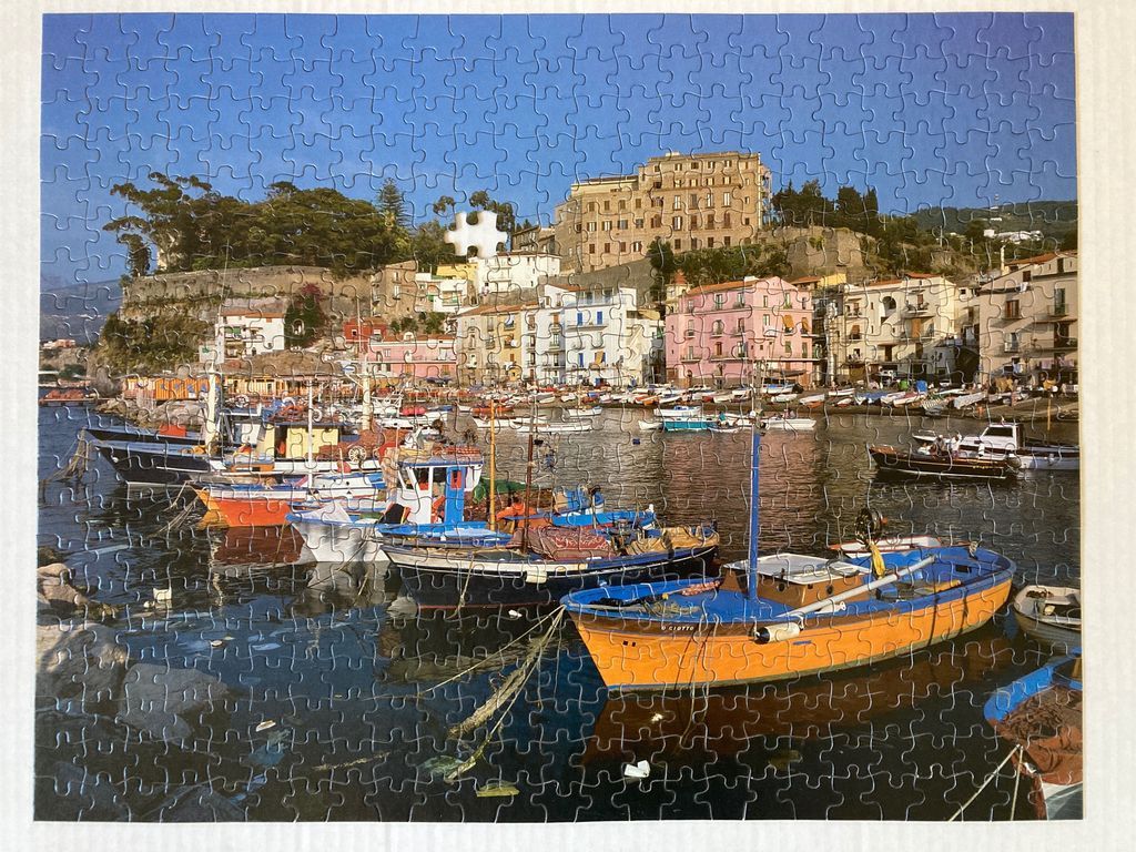 Harbor scene in an Italian coastal town with colorful boats docked in front of hillside buildings.
