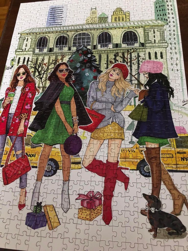Four fashionable women standing in front of a New York City building with a yellow taxi and a small dog.