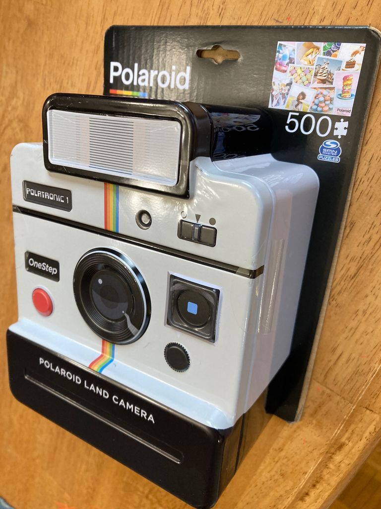 A vintage-style instant film camera with iconic rainbow stripe and light grey housing.