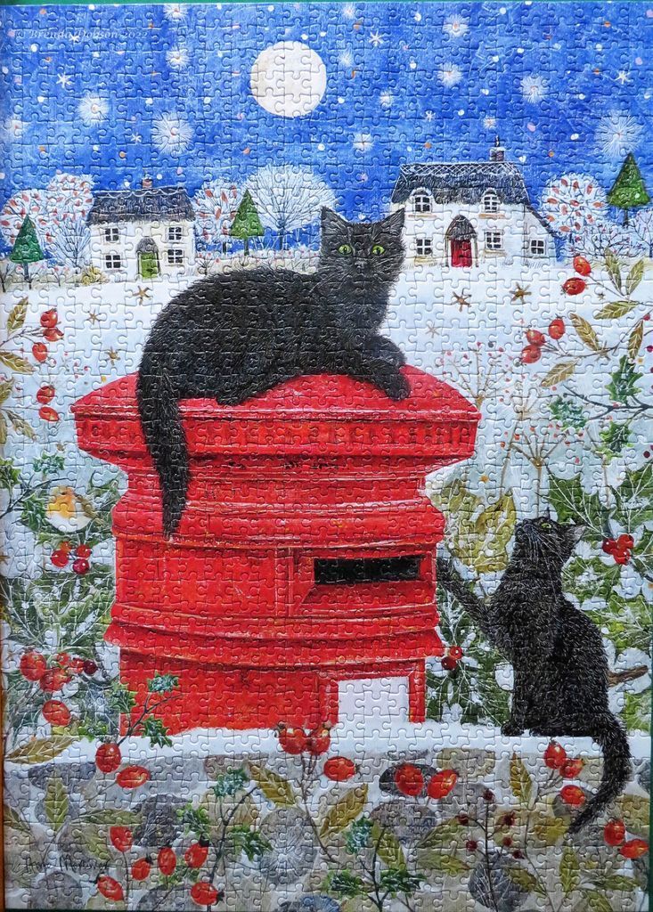 Two black cats near a bright red post box in a snowy, star-filled winter scene at night.