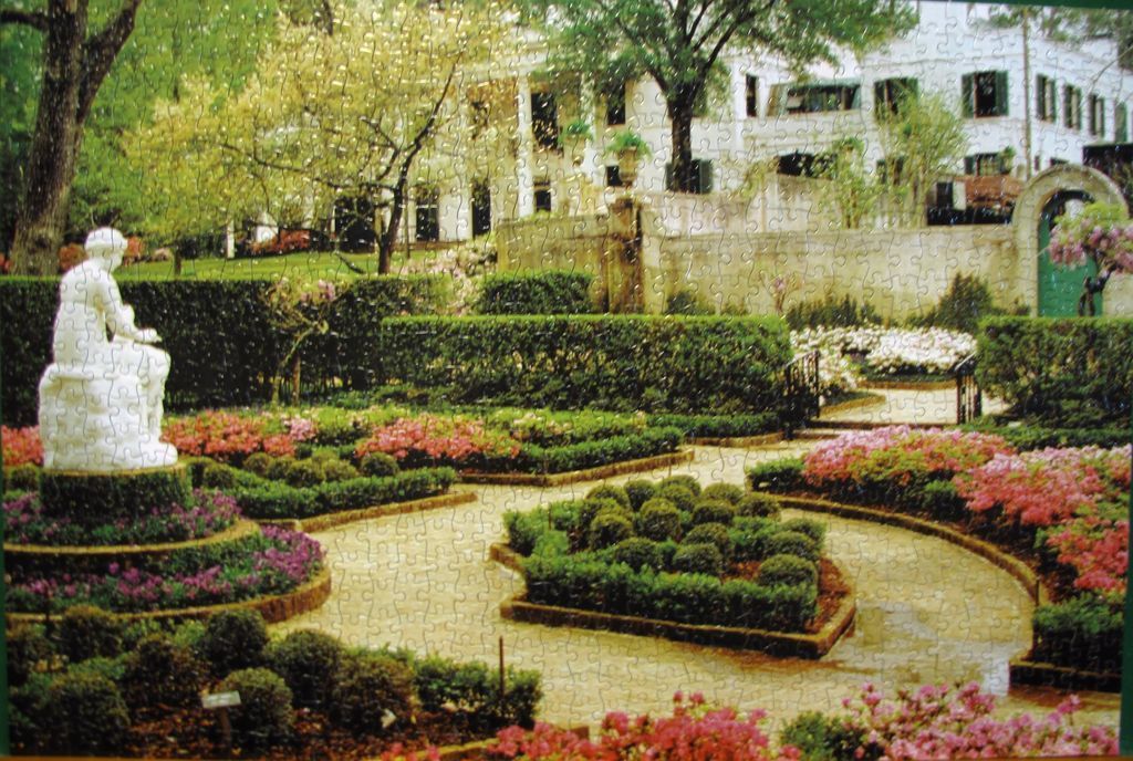 A stately white mansion viewed from a tiered garden with a white stone statue in the foreground.